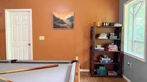 A pool table in a room with a wooden bookshelf and a framed picture on the wall.