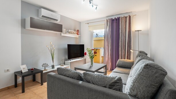 A modern living room with a sofa, TV, and a small table with a vase.