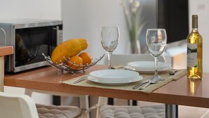 A dining table with a microwave, fruit bowl, wine glasses, and a bottle of wine.