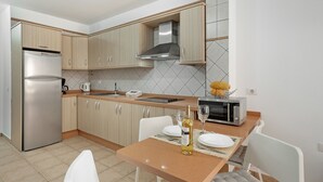 A modern kitchen with a refrigerator, microwave, and a dining table set with plates and a wine bottle.