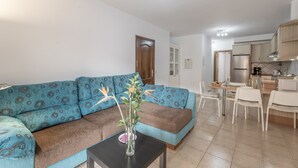 A living room with a sofa, a small table with a vase, and a kitchen area with a refrigerator and cabinets.
