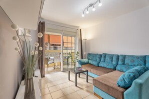 Una sala de estar con sofá, una mesita, un jarrón con plantas y vistas a un espacio exterior a través de un ventanal.
