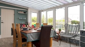 Un coin repas avec une table dressée pour deux personnes, des chaises en bois et un fauteuil en osier.