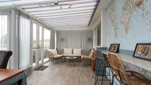 Une pièce dotée d’une grande fenêtre, d’un canapé, de fauteuils, d’un bureau et d’une carte du monde accrochée au mur.