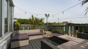 Une terrasse extérieure dotée d’un espace salon, de guirlandes lumineuses et d’une pergola.