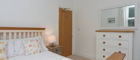 A bedroom with a bed, bedside table, lamp, wooden dresser, and a mirror.