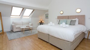 Quarto moderno com uma cama grande, um sofá e uma mesa pequena. Possui claraboias e um lustre.