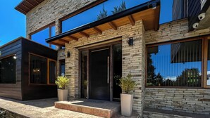 A modern two-story house with a stone facade, large windows, and a wooden overhang. - Apartments Bariloche - Lago Gutierrez (San Carlos de Bariloche)