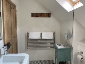 A bathroom with a bathtub, a towel rack with two towels, a small mirror, and a toilet paper holder. - The Shed (Stratford-upon-Avon)