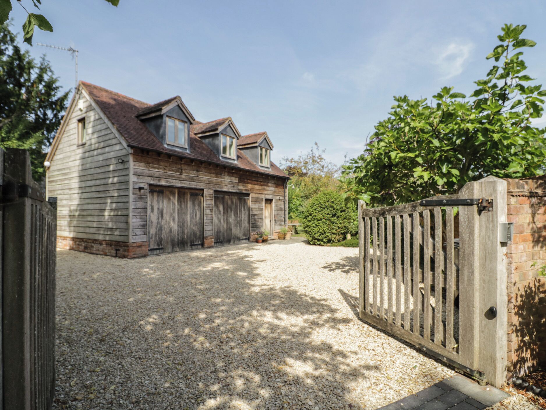 A wooden house with a gravel driveway and a gated entrance.