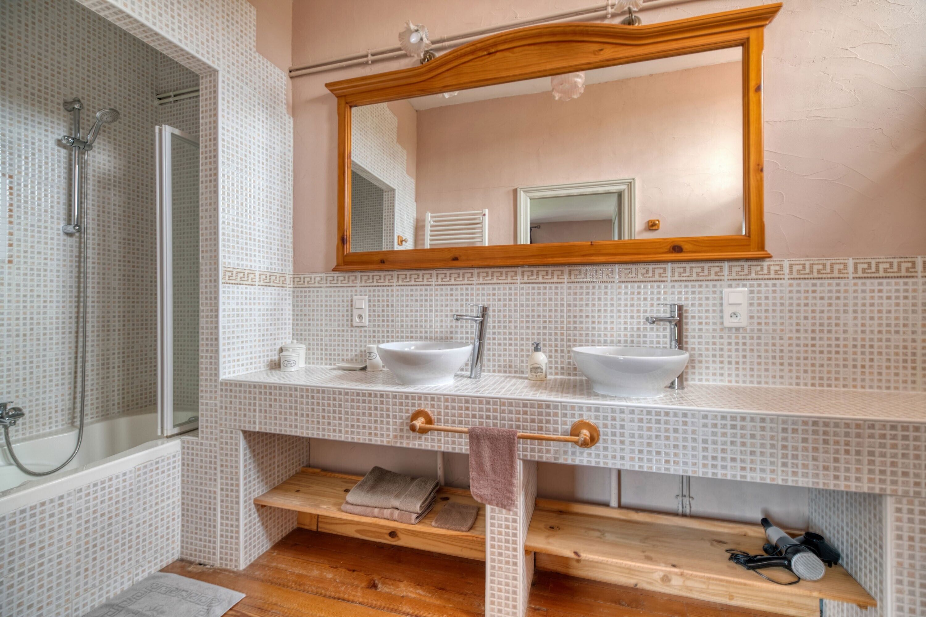 A bathroom with a shower, two sinks, a mirror, and a towel rack.