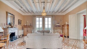 Una habitación con chimenea, un sofá, una araña y vistas a través de las ventanas.