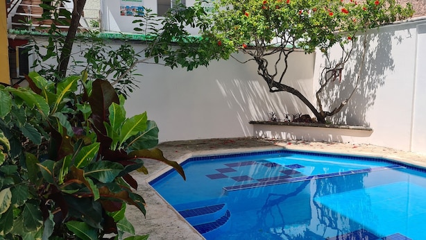 A swimming pool with a tiled edge, surrounded by plants and a tree with red flowers. - Stay 5 min from the beach and downtown Cancun. (Cancún)