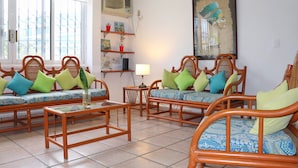 A living room with four wooden sofas with patterned cushions, a glass coffee table, and a wall-mounted air conditioner. - Stay 5 min from the beach and downtown Cancun. (Cancún)