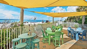 A covered outdoor seating area with tables and chairs, overlooking a beach.