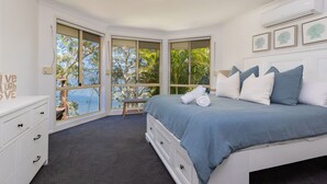 A bedroom with a bed, a nightstand, a dresser, and a window with a view of trees and the sky. - Luminara Luxury Lakefront (Smiths Lake)