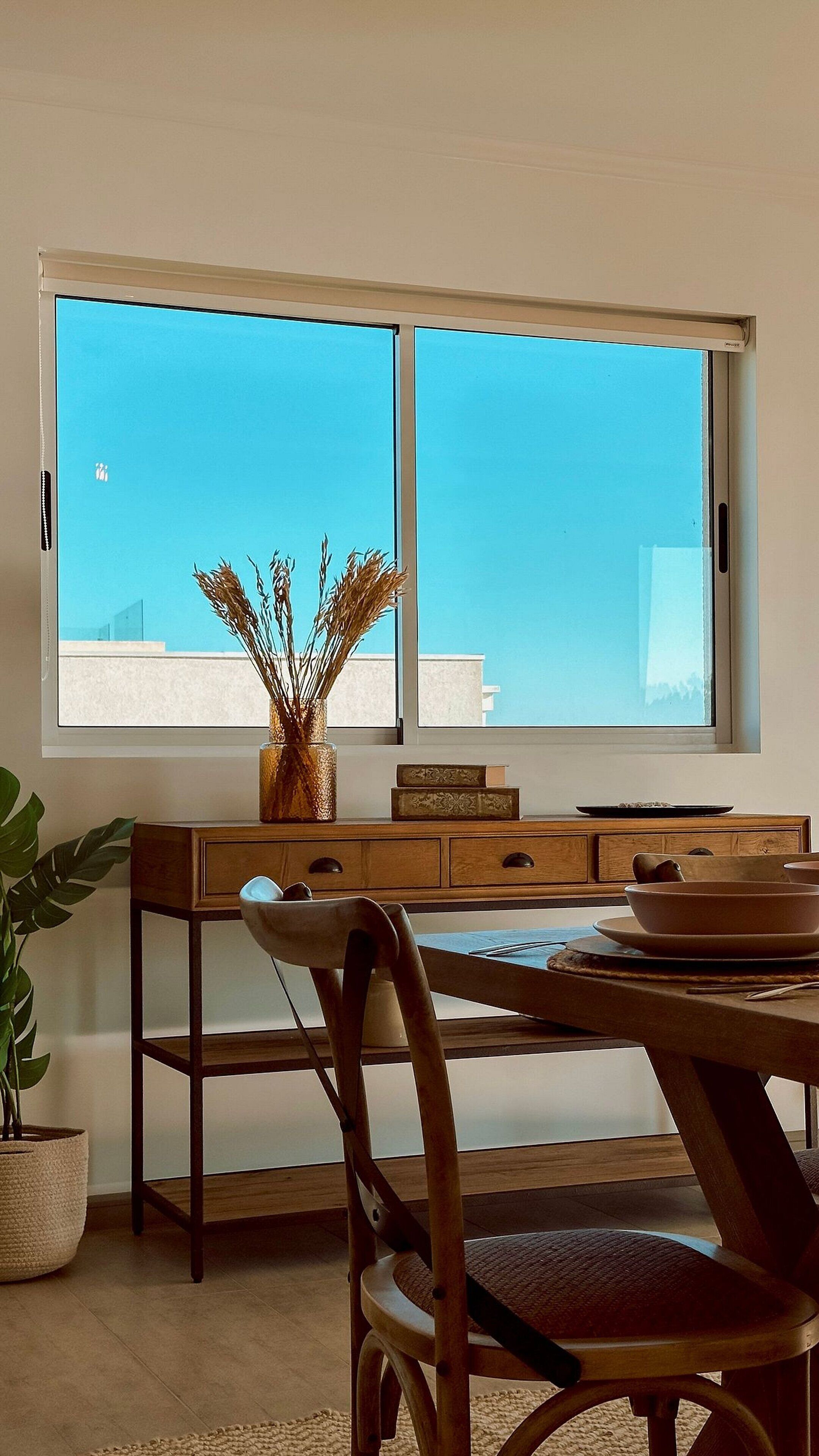 Un coin repas avec une table en bois, des chaises et une grande fenêtre donnant sur le ciel.
