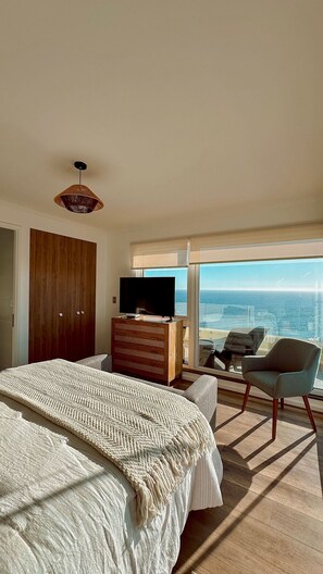 Ein Schlafzimmer mit einem großen Bett, einem Fernseher, einer hölzernen Kommode und Meerblick.