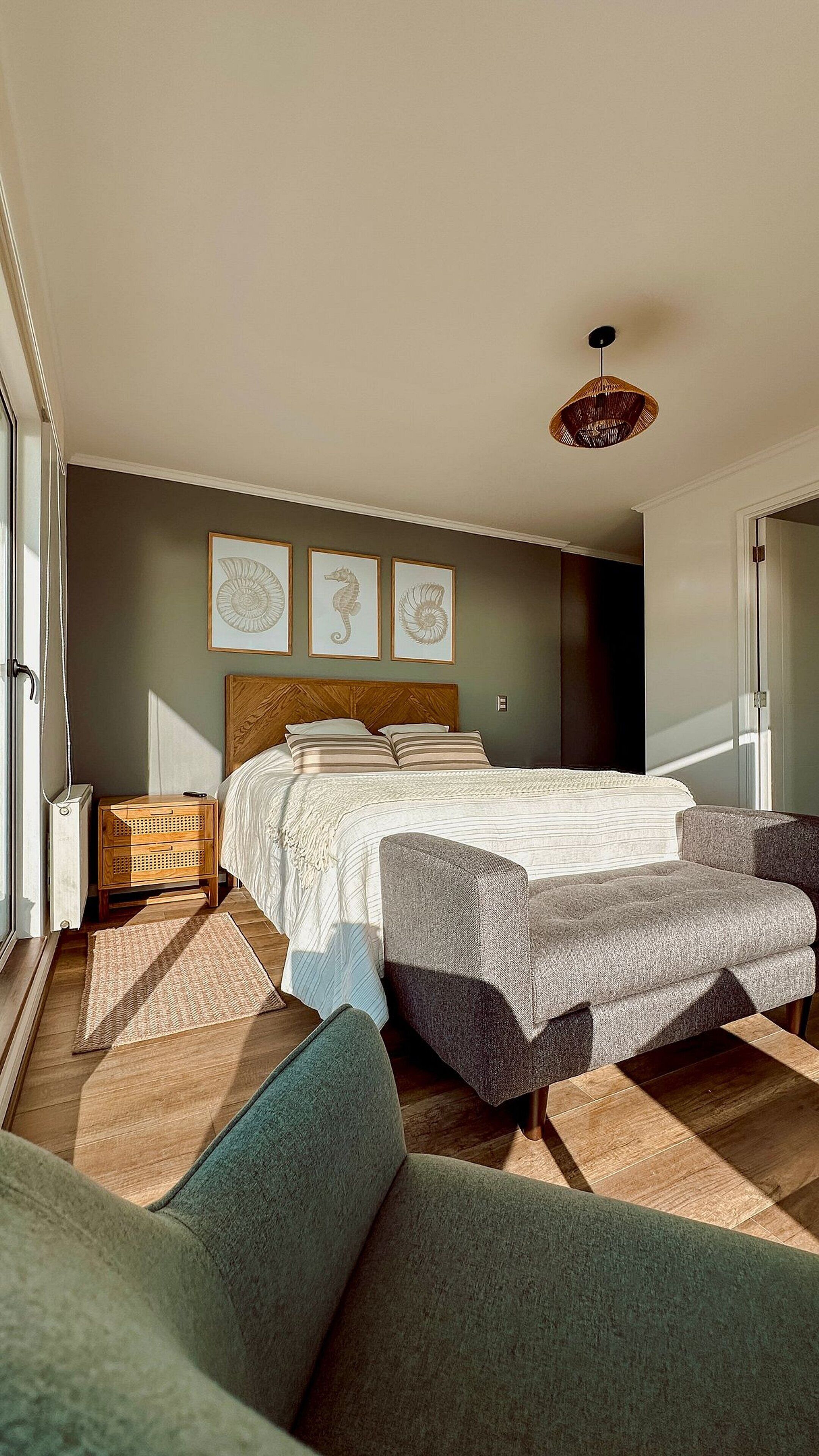 Un dormitori amb un llit, una tauleta de nit, una cadira i una làmpada penjant.