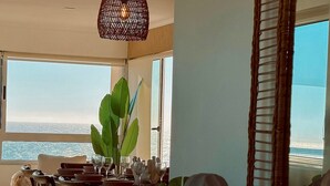 Ein Essbereich mit Blick auf das Meer, einer Korbstuhl-Pendelleuchte und einem großen Spiegel.