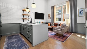 Eine moderne Küche mit einer zentralen Kochinsel, einem Essbereich mit Sofa und Tisch sowie einem großen Fenster mit Vorhängen.