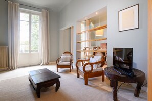 A living room with a sofa, two armchairs, a coffee table, a TV on a stand, and a bookshelf.