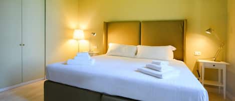 A neatly made bed with white linens and towels, two bedside lamps, and a small bedside table.