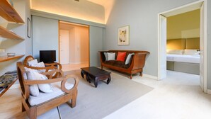 Ein Wohnzimmer mit einer Couch, einem Holztisch und einem Fernseher. Eine Tür führt zu einem Schlafzimmer.