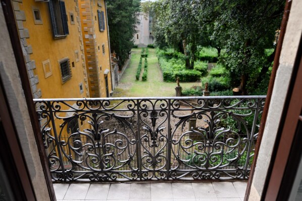 Un balcón con barandilla de hierro forjado decorativa que da a un jardín cuidado y un edificio de paredes amarillas.