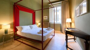 Ein Bett mit Baldachin, weiße Bettwäsche, ein Nachttisch mit Lampe und ein Fenster mit Vorhängen.
