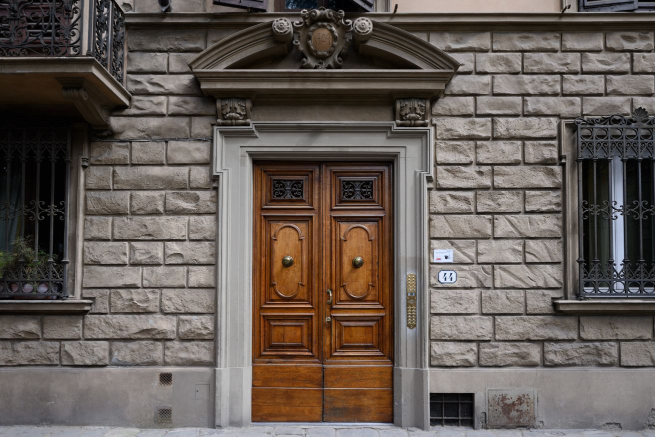 A double wooden door with a brass handle, flanked by stone walls and ornate metal railings.