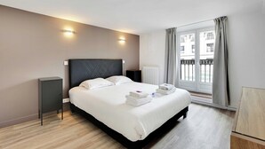 A modern hotel room with a large bed, bedside tables, a radiator, and a window with curtains. - Charming Apartment- 3br-8p Opera (Paris)
