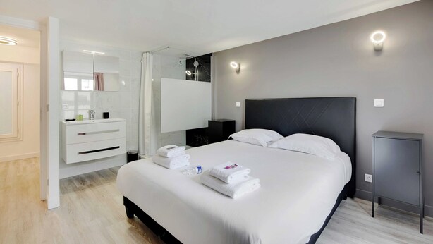 A modern hotel room with a large bed, a bedside table, a wardrobe, and a mirror. - Charming Apartment- 3br-8p Opera (Paris)