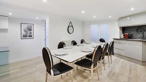 A modern dining area with a rectangular table set for six, surrounded by chairs with black cushions. A wall-mounted clock is visible above the table. - Charming Apartment- 3br-8p Opera (Paris)