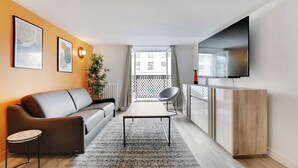 A modern living room with a sofa, a coffee table, a TV, and a balcony with a view of buildings. - Charming Apartment- 3br-8p Opera (Paris)