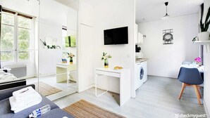A modern hotel room with a large bed, a desk, a washing machine, and a TV. - Studio in the Heart of the Marais (Paris)