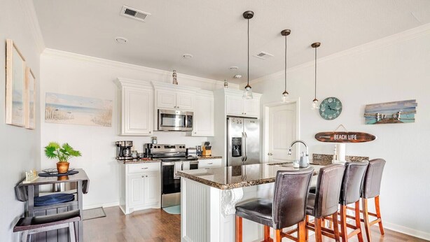 A modern kitchen with white cabinetry, stainless steel appliances, and a bar area with leather chairs.
