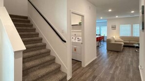 Un intérieur moderne avec un escalier recouvert de moquette, un espace de vie doté d’un canapé et une cuisine équipée.