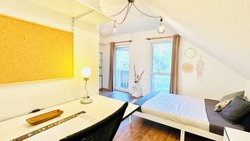 Ein Schlafzimmer mit Bett, Schreibtisch, Stuhl und Blick ins Freie durch ein Fenster.