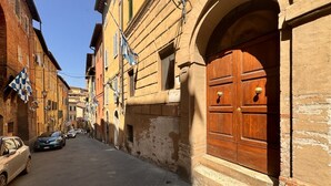 A narrow street with historic buildings, a wooden door, and parked cars. - Dimora with a view of the Torre del Mangia (Siena)