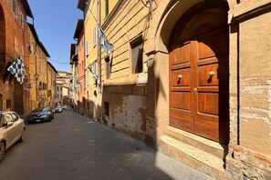 A narrow street with historic buildings, a wooden door, and parked cars.