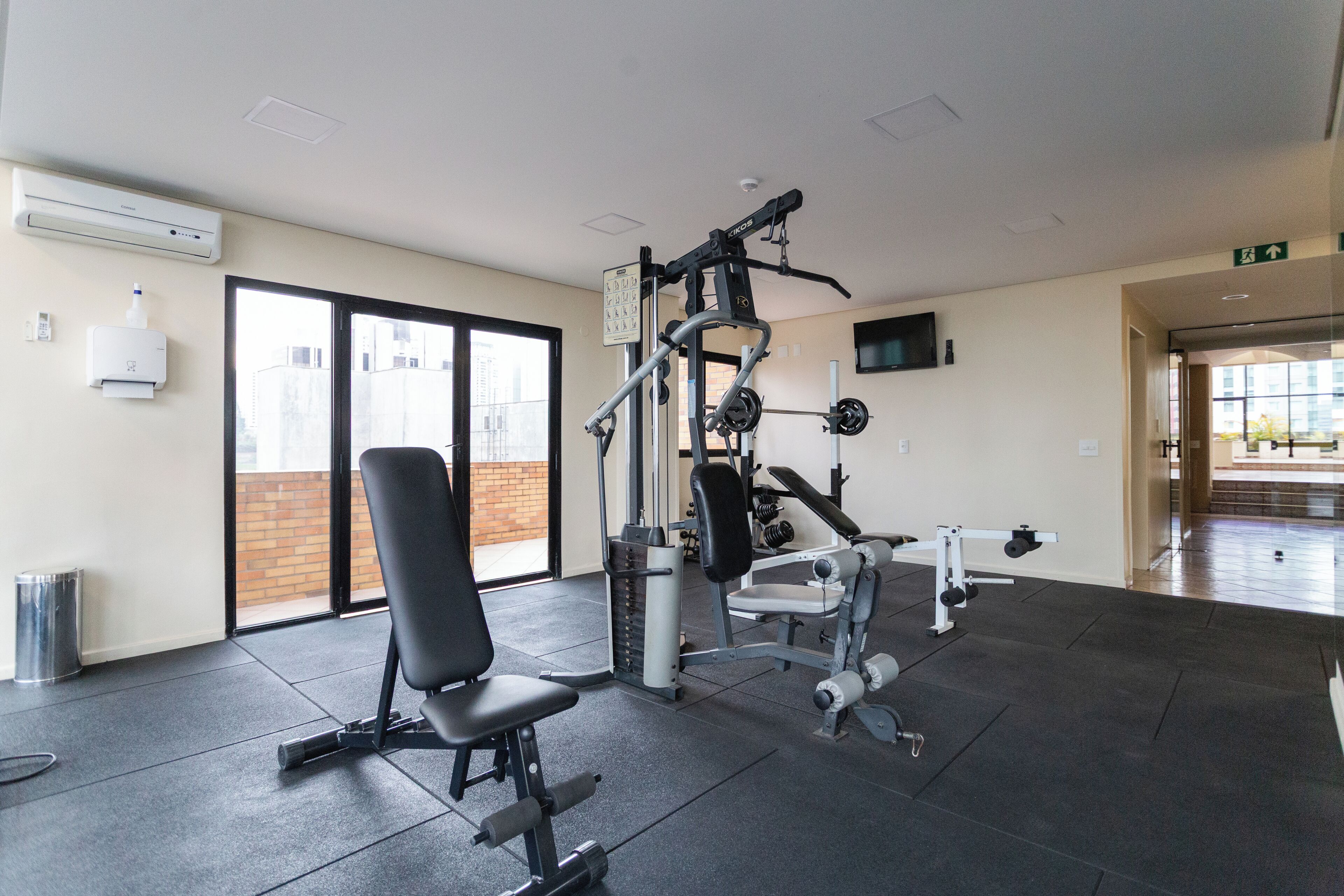 Ein Fitnessstudio mit Trainingsgeräten, einem schwarzen Stuhl und einem großen Fenster.