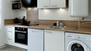A modern kitchen with white cabinetry, a built-in oven, a dishwasher, a washing machine, and a hanging light fixture.