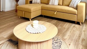 A modern living room with a yellow sectional sofa, a round wooden coffee table, and a decorative wall piece.