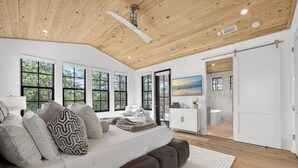 A spacious room with a large bed, wooden ceiling, and large windows.