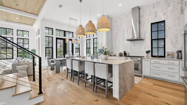 A modern kitchen with a central island, large windows, and a staircase leading to a loft area.