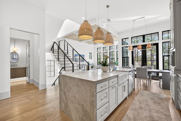 A modern kitchen with a large island, pendant lights, and a staircase leading to a loft area.