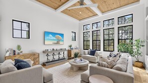A spacious living room with a high ceiling, large windows, and a cozy seating area.