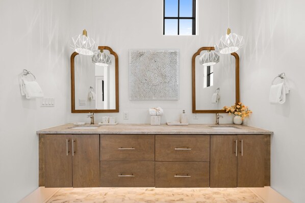 Un baño moderno con dos espejos grandes, un mueble de tocador de madera y una ventana sobre los espejos.