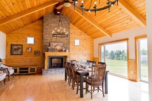 L’intérieur d’une cabane en rondins comprend un coin repas, une cheminée et de grandes fenêtres.